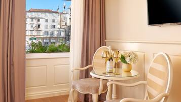 Una habitación con vistas a edificios históricos, una mesa redonda de vidrio con dos sillas, un jarrón de flores y una botella de champán.