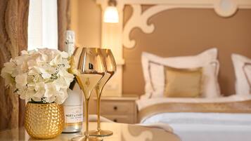 Una cama con ropa blanca, una mesita de noche con una botella de champán y dos copas, y un jarrón con flores blancas.