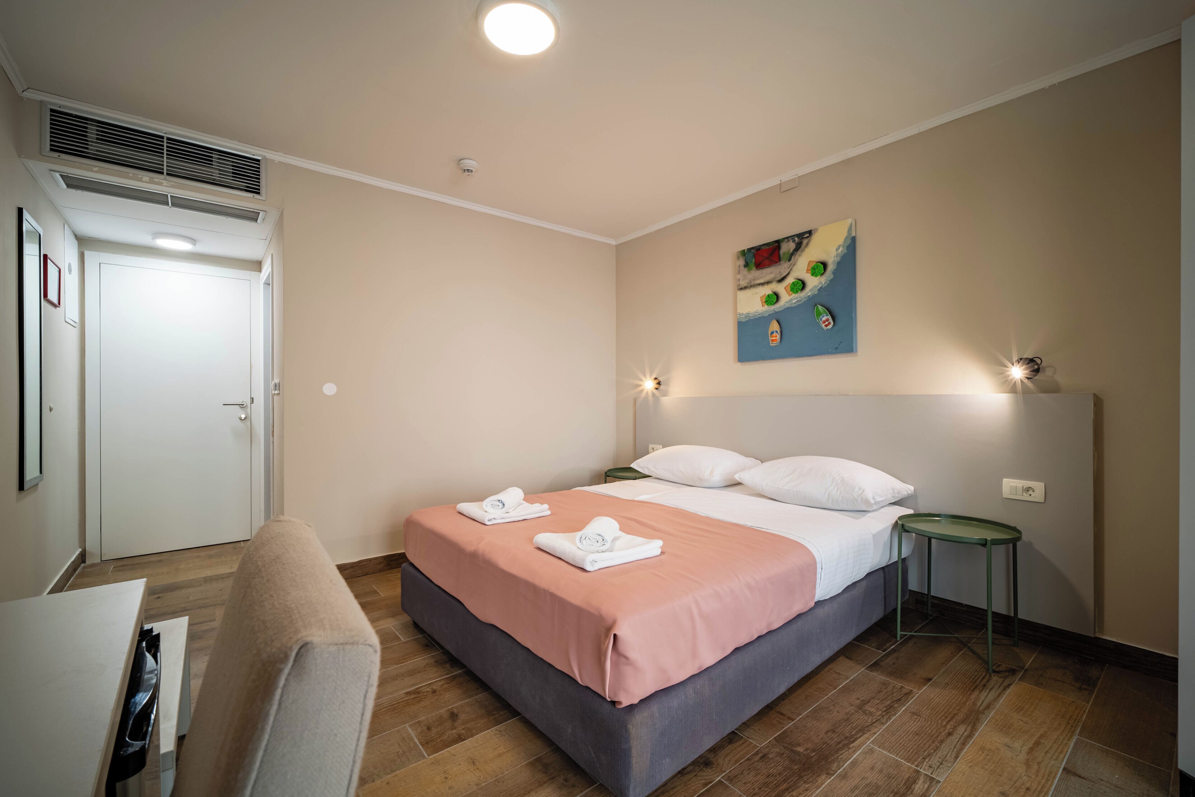 Une chambre d’hôtel comprenant un lit, un bureau, une chaise, une petite table, une œuvre d’art murale et une porte.