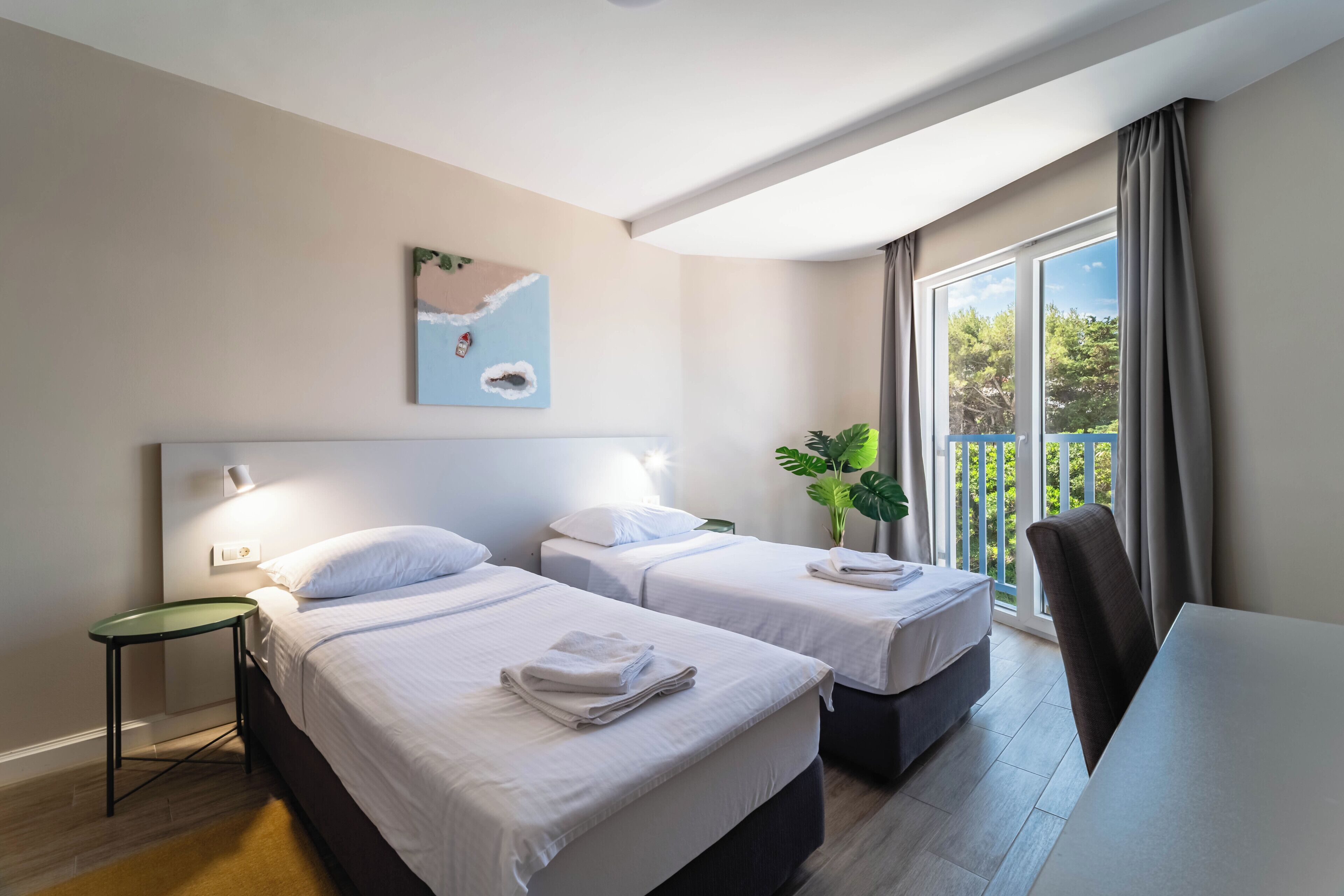Habitación de hotel con dos camas, una mesa de comedor, una silla, una mesita y un balcón con planta.