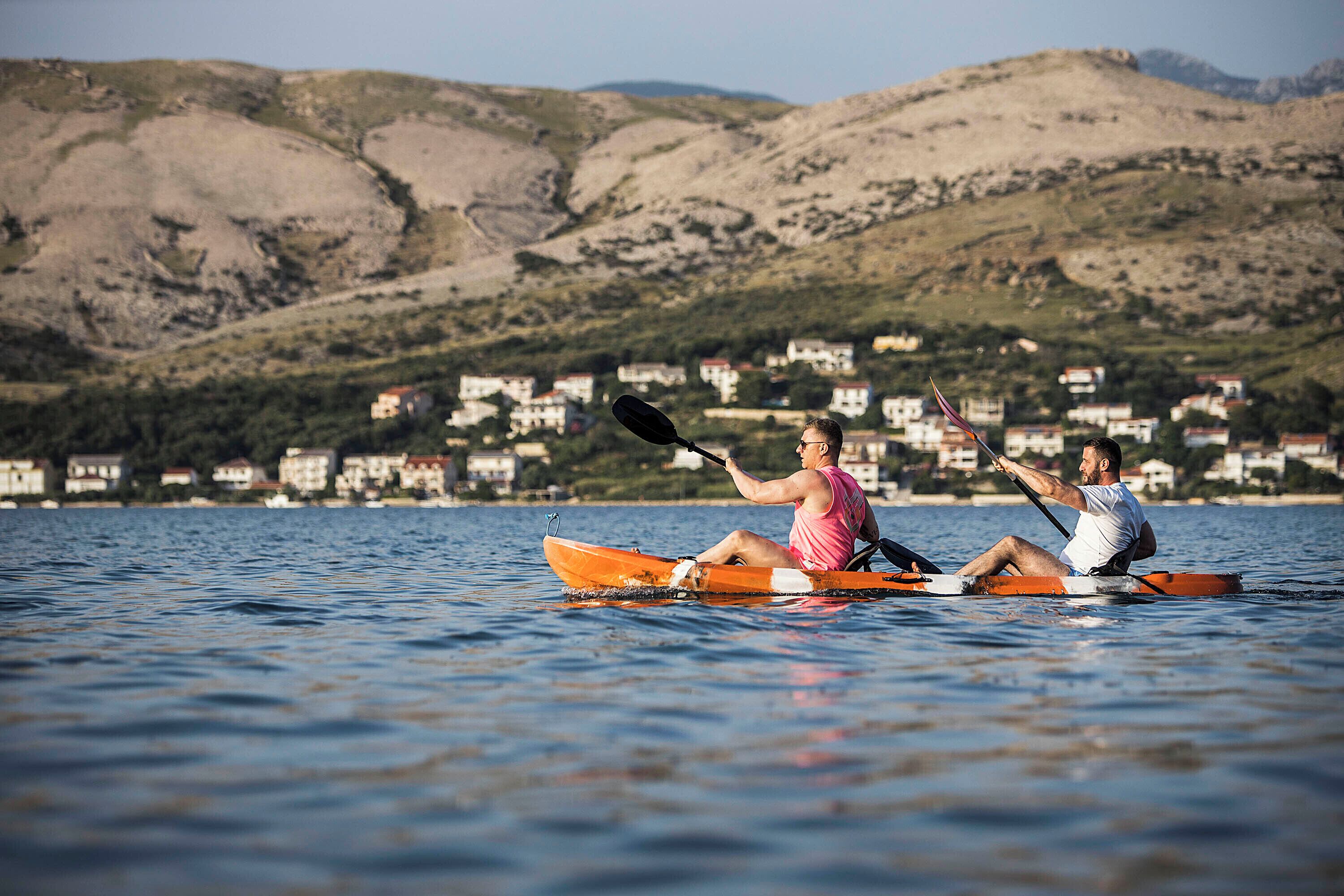 Two people in a canoe on a lake with houses and mountains in the background.