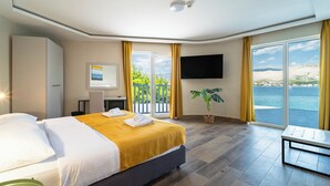 A hotel room with a bed, a desk, a TV, and a balcony with a view of the sea. - Hotel Plaža (Pag)