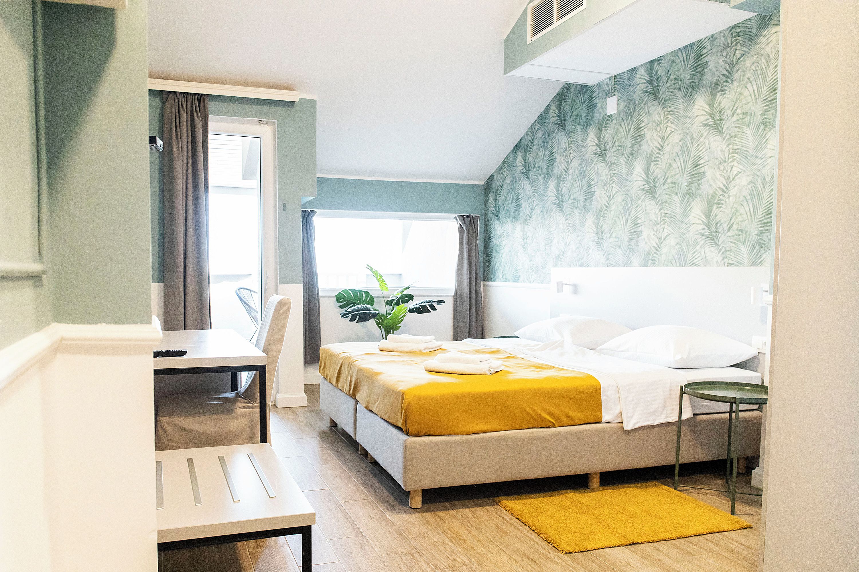 Ein modernes Schlafzimmer mit Bett, Nachttisch, Sessel und einem Fenster mit Vorhängen.