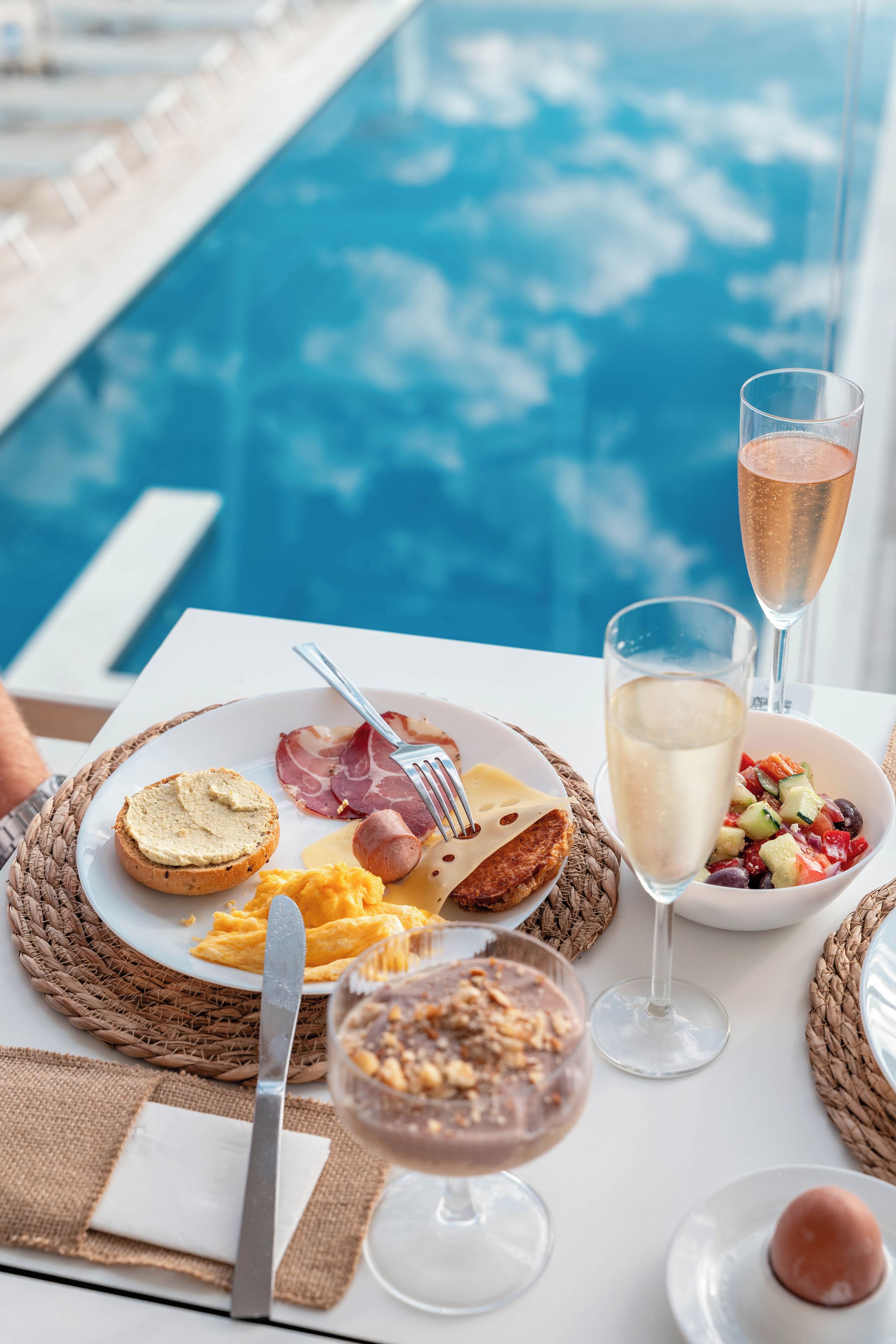 A dining table with breakfast items, a glass of champagne, and a view of a pool.