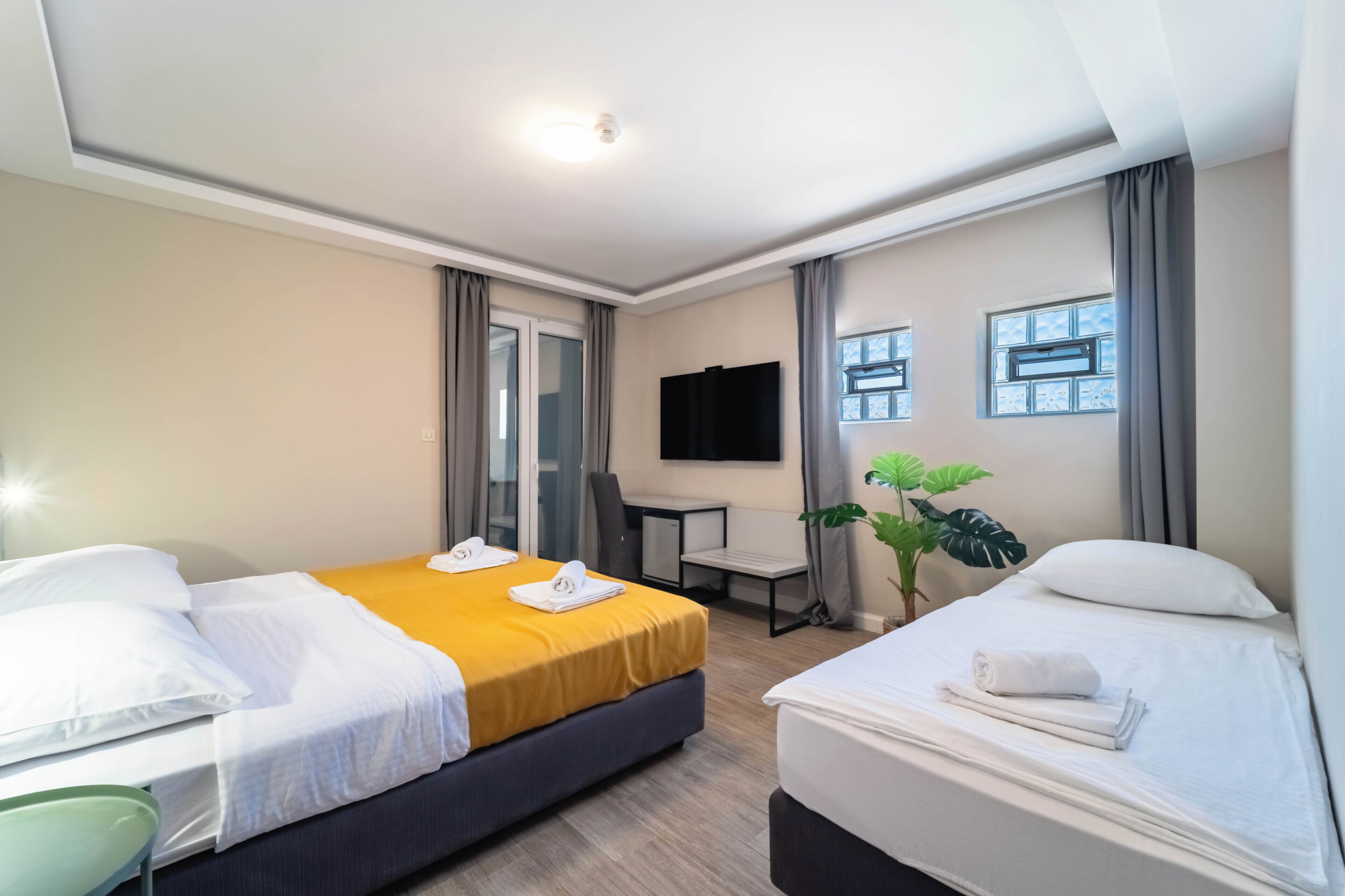 A hotel room with two beds, a desk, a chair, a TV, and a plant.