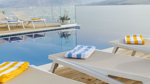A poolside area with lounge chairs, a glass railing, and a view of the water. - Hotel Plaža (Pag)