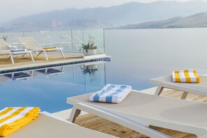 A poolside area with lounge chairs, a glass railing, and a view of the water. - Hotel Plaža (Pag)