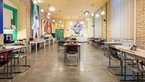 A spacious cafe with wooden floors, multiple tables and chairs, hanging pendant lights, and a large mural on the back wall. - Full Moon Budapest (Budapest)