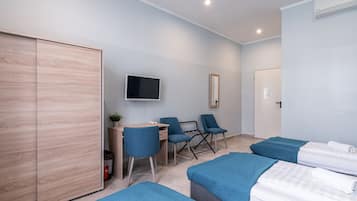 A modern hotel room with a wooden wardrobe, a desk with a chair, a television, and two beds with blue bedding.