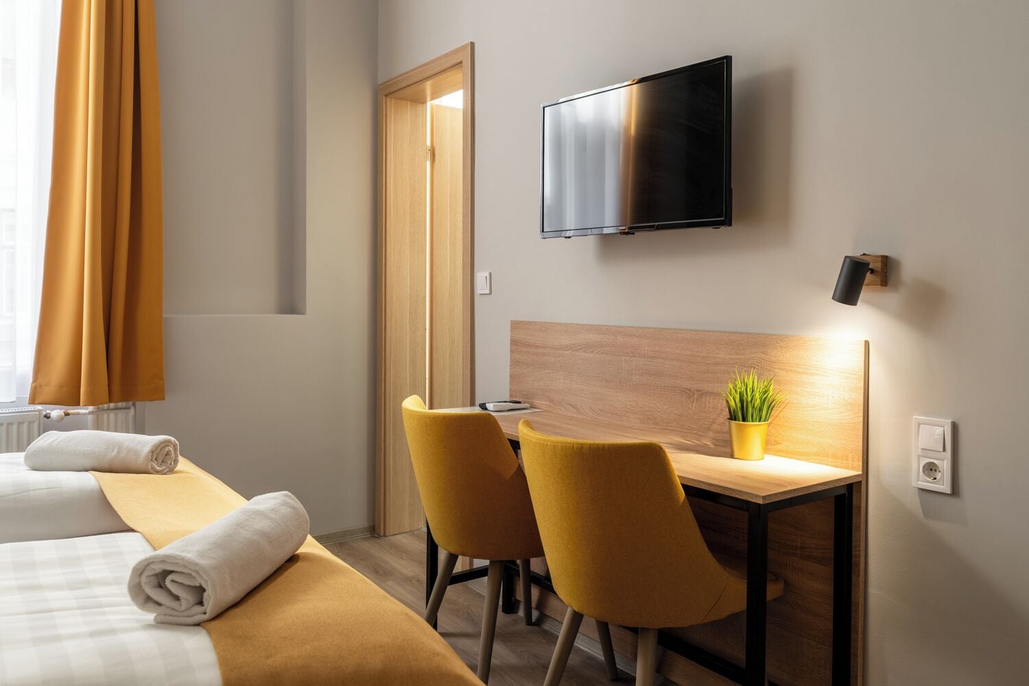 A hotel room with a bed, a desk, two chairs, a television, and a plant.
