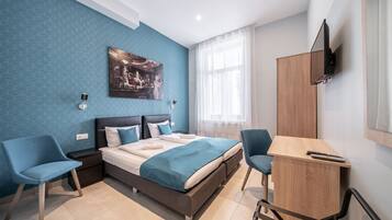 A modern bedroom with a bed, two chairs, a desk, and a TV.