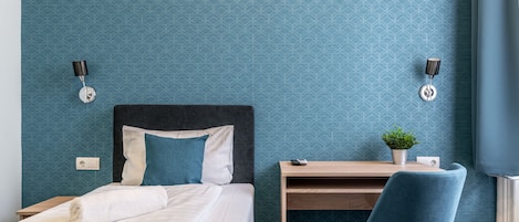 A hotel room with a bed, a desk, a chair, and a wall-mounted lamp.