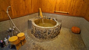 A stone hot tub with a wooden interior, a stone floor, and a wooden wall. - Hot Spring Inn Banya (Yufu)
