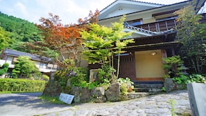 A traditional Japanese house with a stone pathway leading to the entrance, surrounded by lush greenery and autumn foliage. - Hot Spring Inn Banya (Yufu)