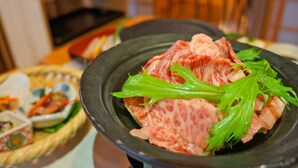 A dining table with a black plate containing sliced meat and green garnish. - Hot Spring Inn Banya (Yufu)