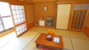 A traditional Japanese room with tatami flooring, a low wooden table with a red cushion, a television, and a small refrigerator. - Hot Spring Inn Banya (Yufu)