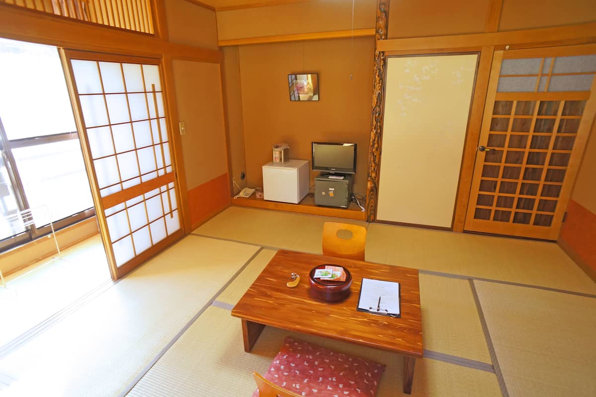 A traditional Japanese room with tatami flooring, a low wooden table with a red cushion, a television, and a small refrigerator.
