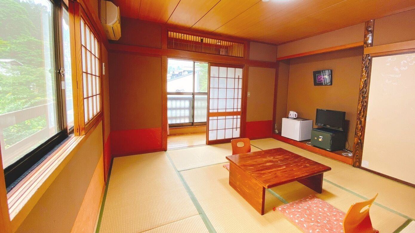 A traditional Japanese room with tatami flooring, a wooden table, a TV, and a refrigerator.