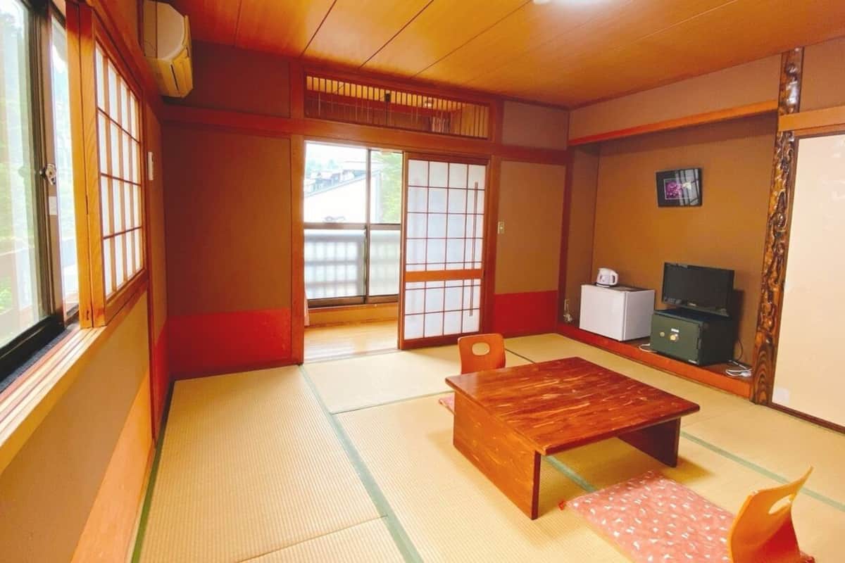 A traditional Japanese room with tatami flooring, a wooden table, a TV, and a refrigerator.