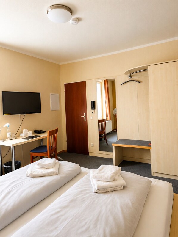 Una habitación de hotel con dos camas, un escritorio, una silla, un televisor y un armario.