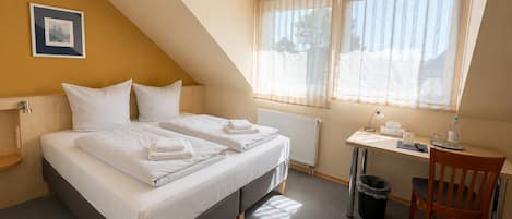 Habitación de hotel con dos camas, un escritorio, una silla, un radiador y un cuadro en la pared.