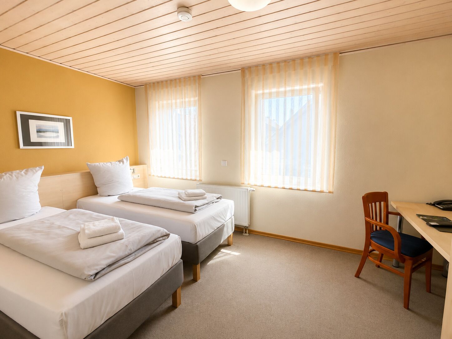 Une chambre d’hôtel avec deux lits, un bureau, une chaise et un radiateur.