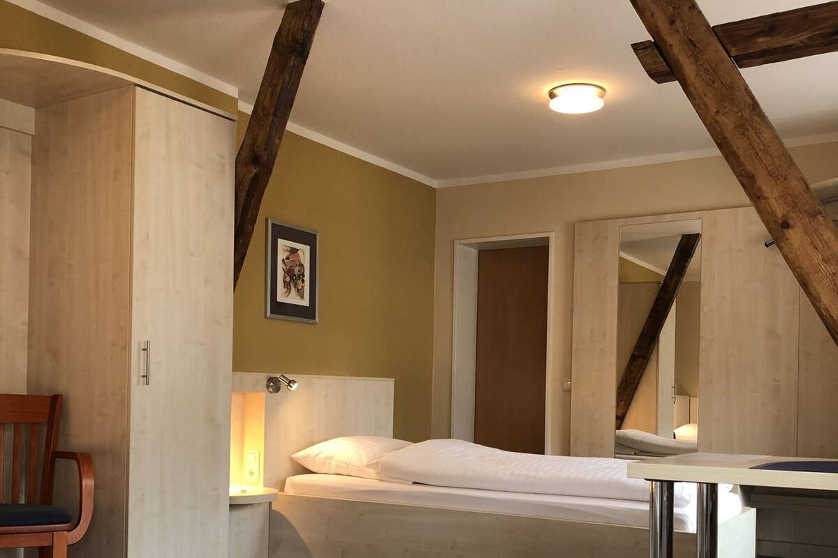 A bedroom with a bed, a chair, a desk, and a mirror.