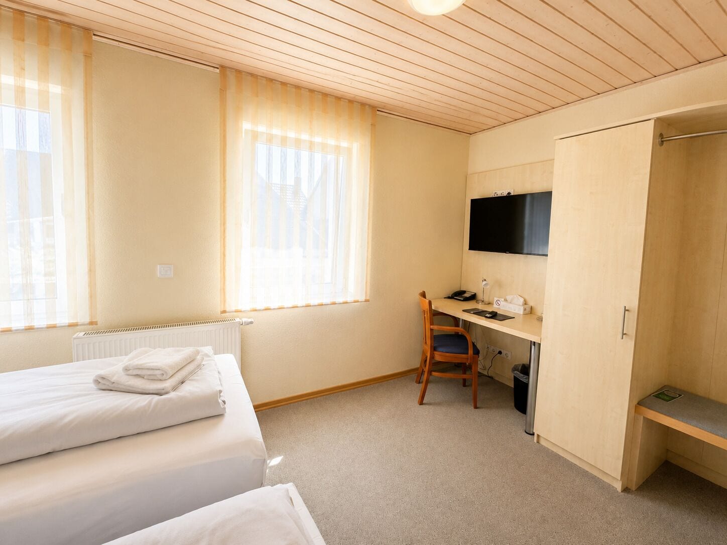 Une chambre d’hôtel avec deux lits, un bureau avec une chaise, une télévision et une armoire.