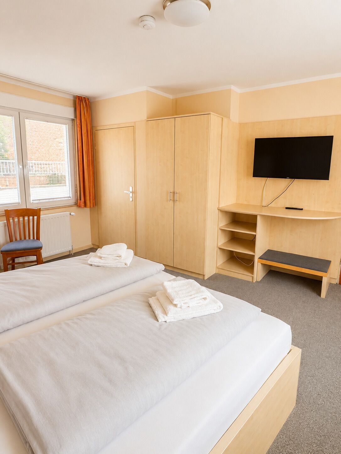 Quarto de hotel com duas camas, televisão, escrivaninha e uma cadeira.