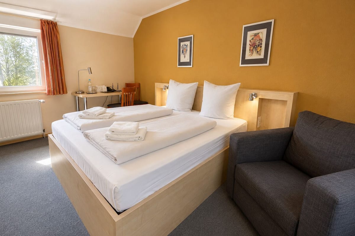 A hotel room with a large bed, a desk, a chair, and a sofa.