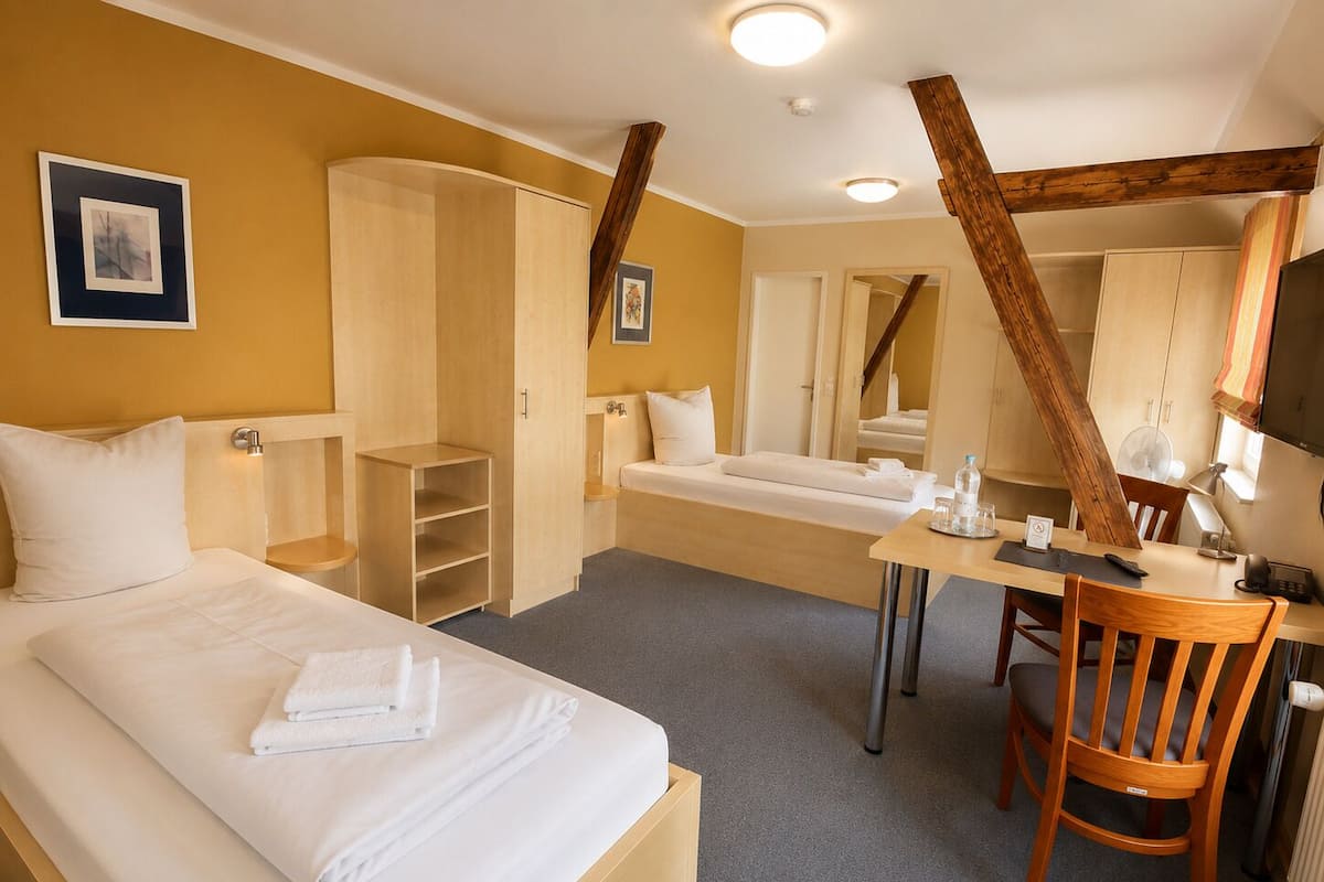 A hotel room with two beds, a desk, a chair, a wardrobe, and a mirror.