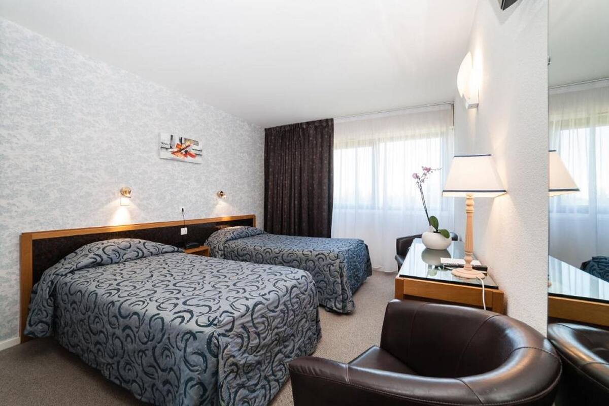 A hotel room with two beds, a desk, a chair, and a mirror.