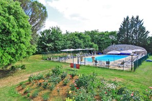 Ein Schwimmbecken mit Liegestühlen und Sonnenschirmen, umgeben von einem Garten mit Blumen und Bäumen.