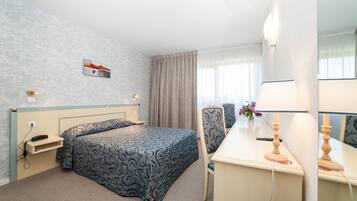 Une chambre d’hôtel avec un lit, un bureau, une chaise, une lampe, un téléphone et un tableau au mur.