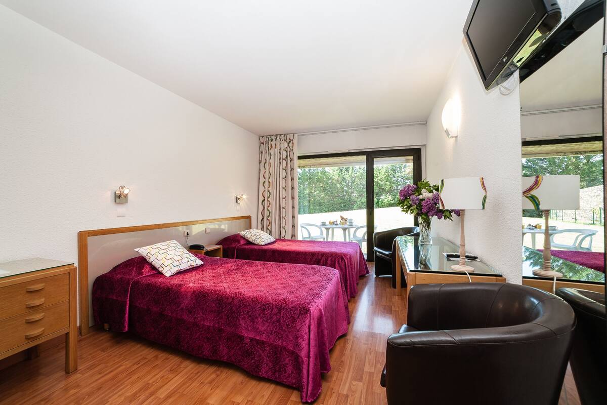 A hotel room with two beds, a desk, a chair, and a TV.