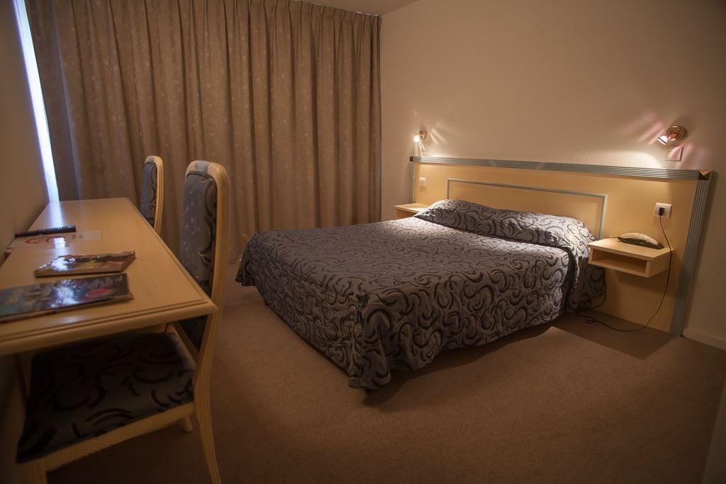 Una habitación de hotel con cama, mesita de noche, lámpara y un escritorio con silla.
