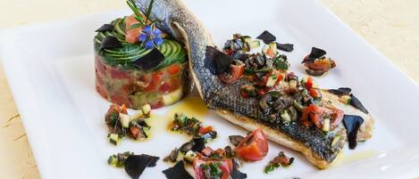 Un plato blanco con un pescado a la plancha y una ensalada colorida.