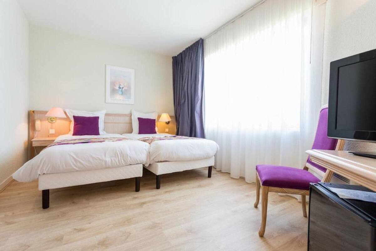A hotel room with two beds, a desk, a chair, a television, and a window with curtains.