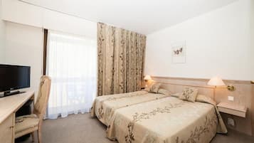 A hotel room with two beds, a desk with a TV, a chair, and a window with curtains.