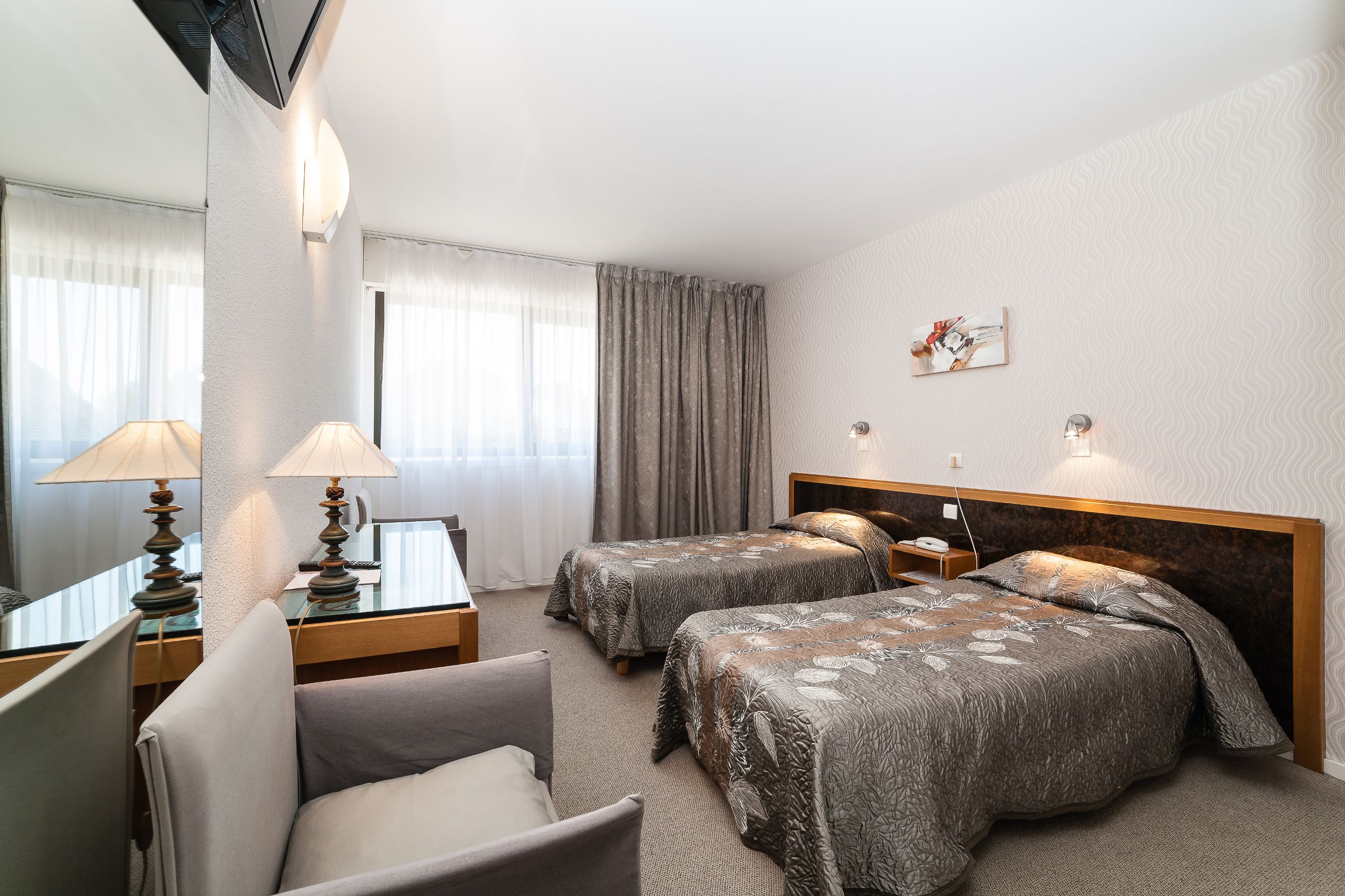 A hotel room with two beds, a chair, a desk, and a mirror.