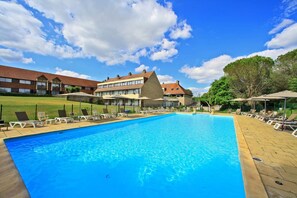 Ein Swimmingpool mit Liegestühlen und ein Gebäude mit einem markanten, dreieckigen Dach im Hintergrund.