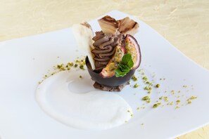 Dessert auf einem weißen Teller mit Schokoladengirlande, einer Frucht und Minzblättern.