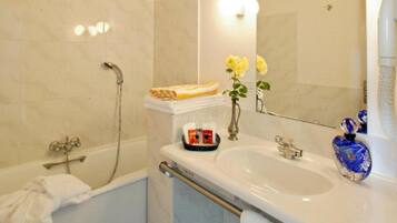 A bathroom with a bathtub, a sink, and a mirror. There is a towel rack, a bottle of soap, and a vase with flowers.
