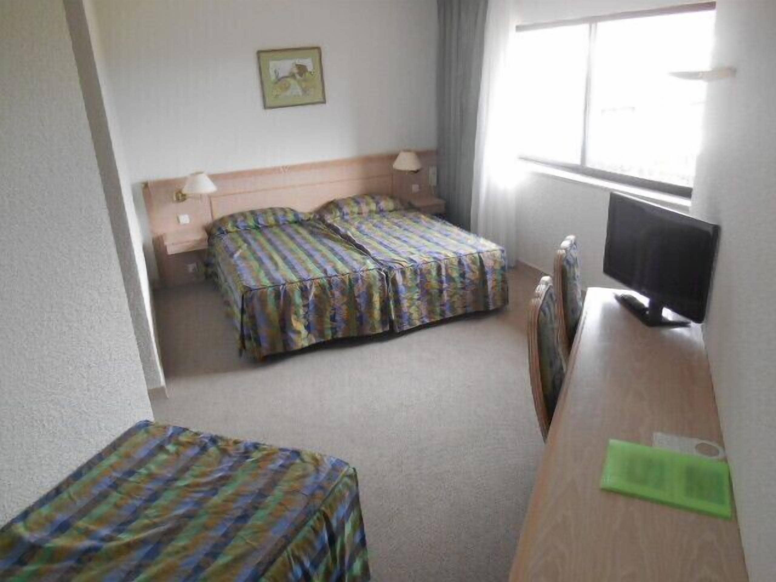Une chambre d’hôtel avec deux lits, une télévision et une fenêtre.