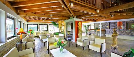 Un vestíbulo amplio con techos altos, vigas de madera y diversas opciones de asientos, incluyendo sofás y sillones.
