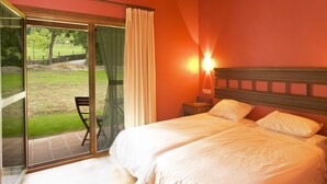 Une chambre avec un grand lit, une table de chevet, une lampe et une porte-fenêtre coulissante donnant sur une terrasse.