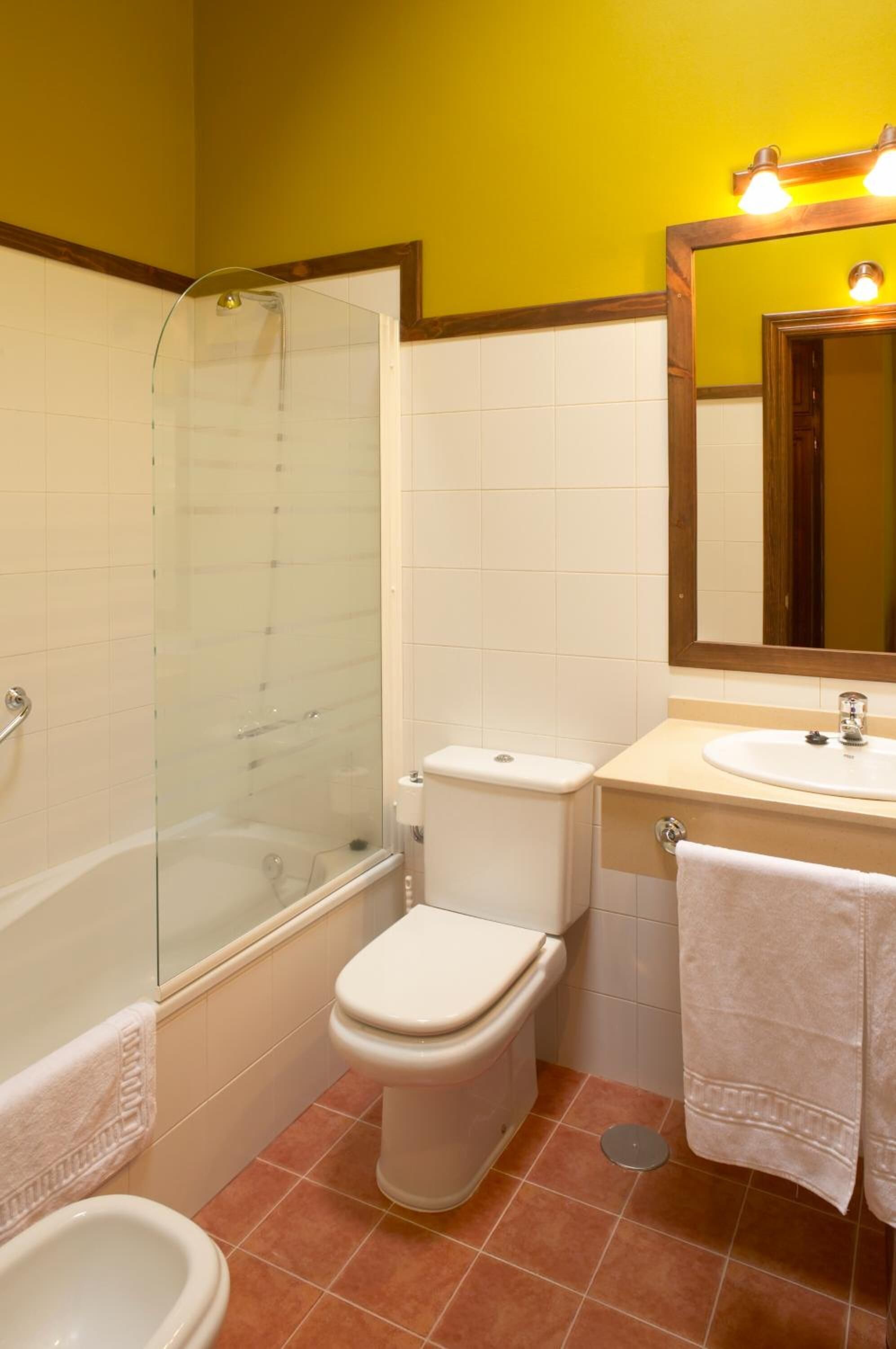 Un baño con ducha acristalada, inodoro, lavamanos y espejo.