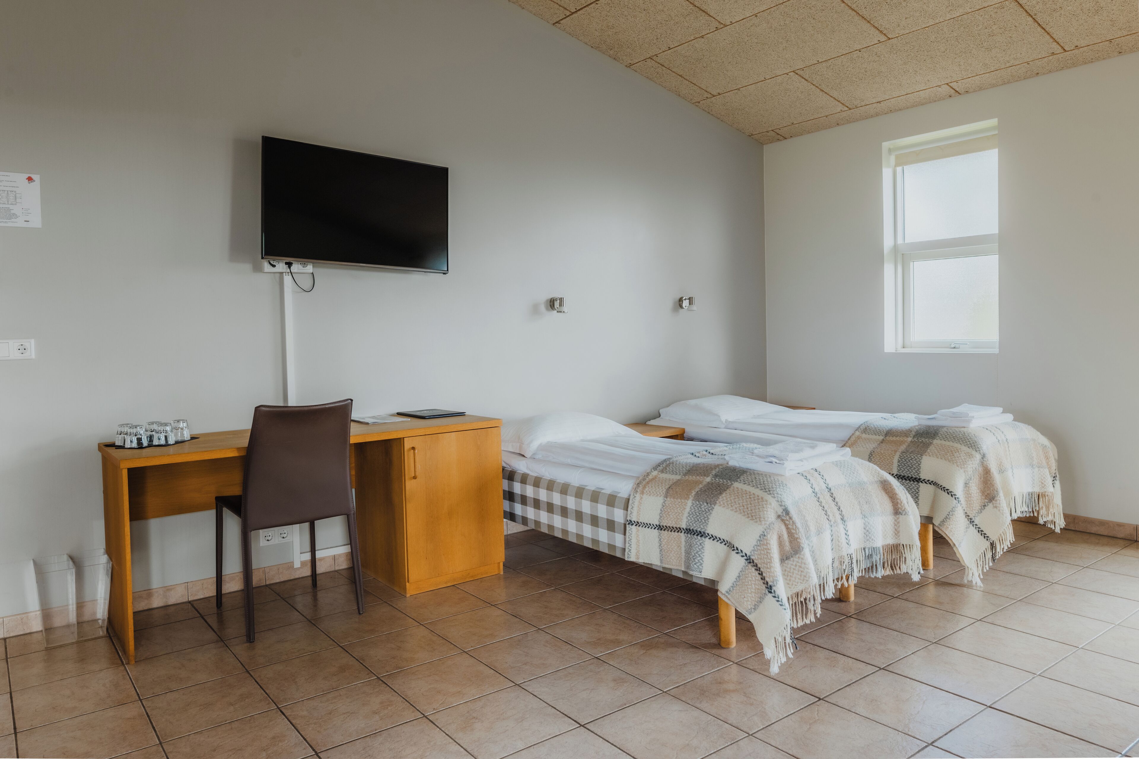 Una habitación con cama, escritorio, silla, televisión y ventana.