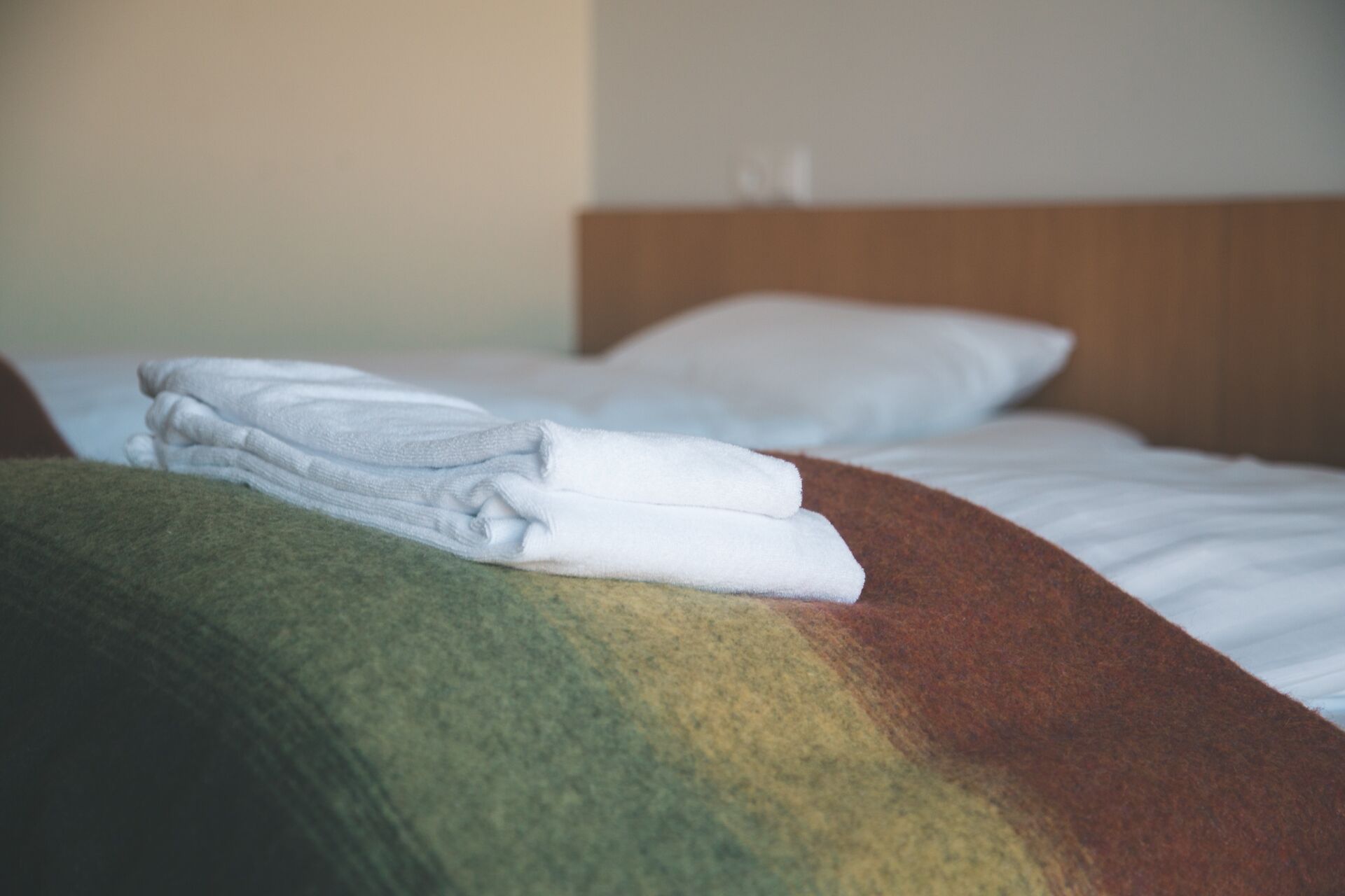 Una cama bien hecha con sábanas blancas y una toalla doblada sobre un edredón de colores.