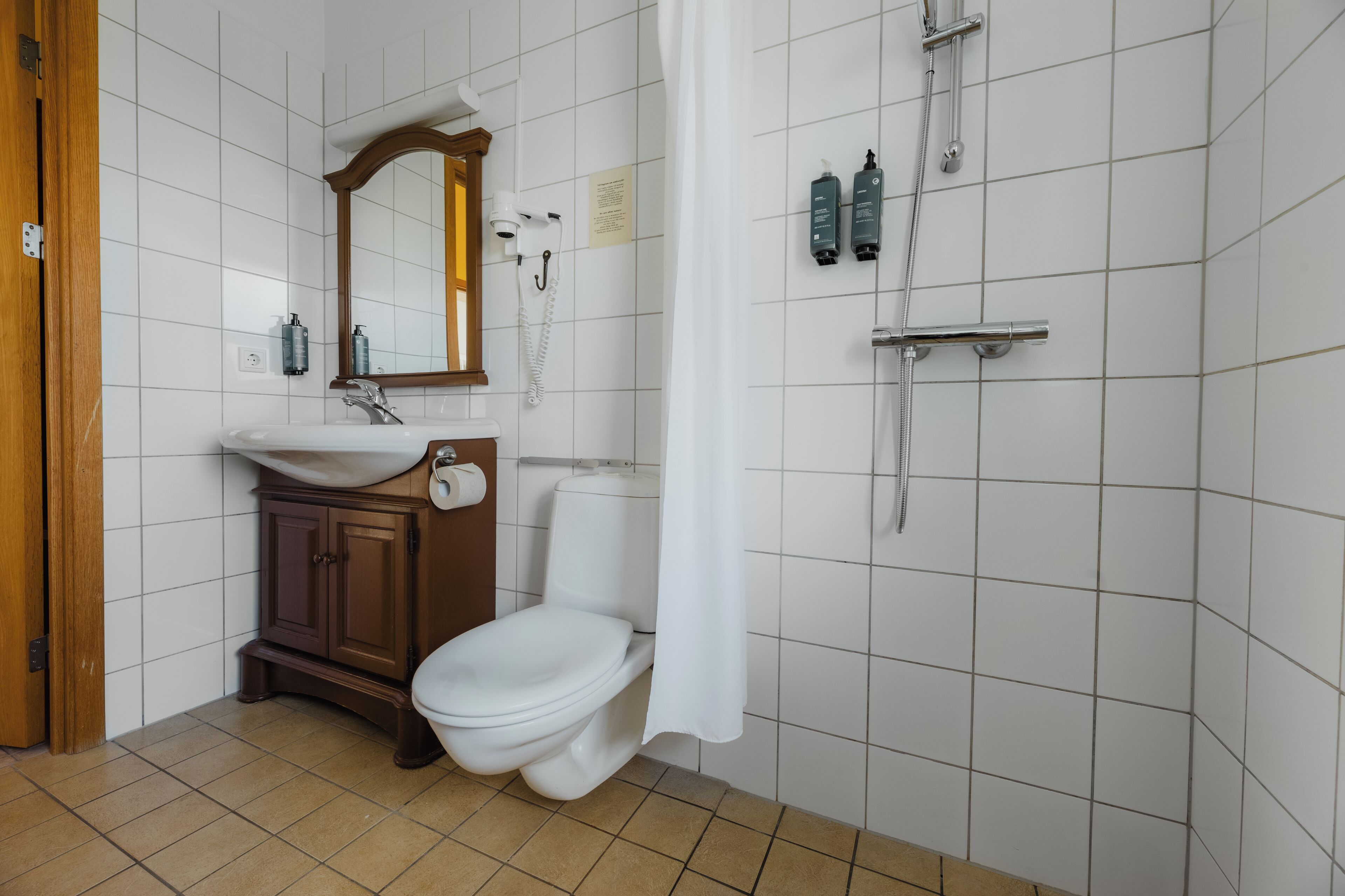 Ein Badezimmer mit weißem Waschbecken, Holzschrank, Toilette und Duschbereich mit Vorhang.